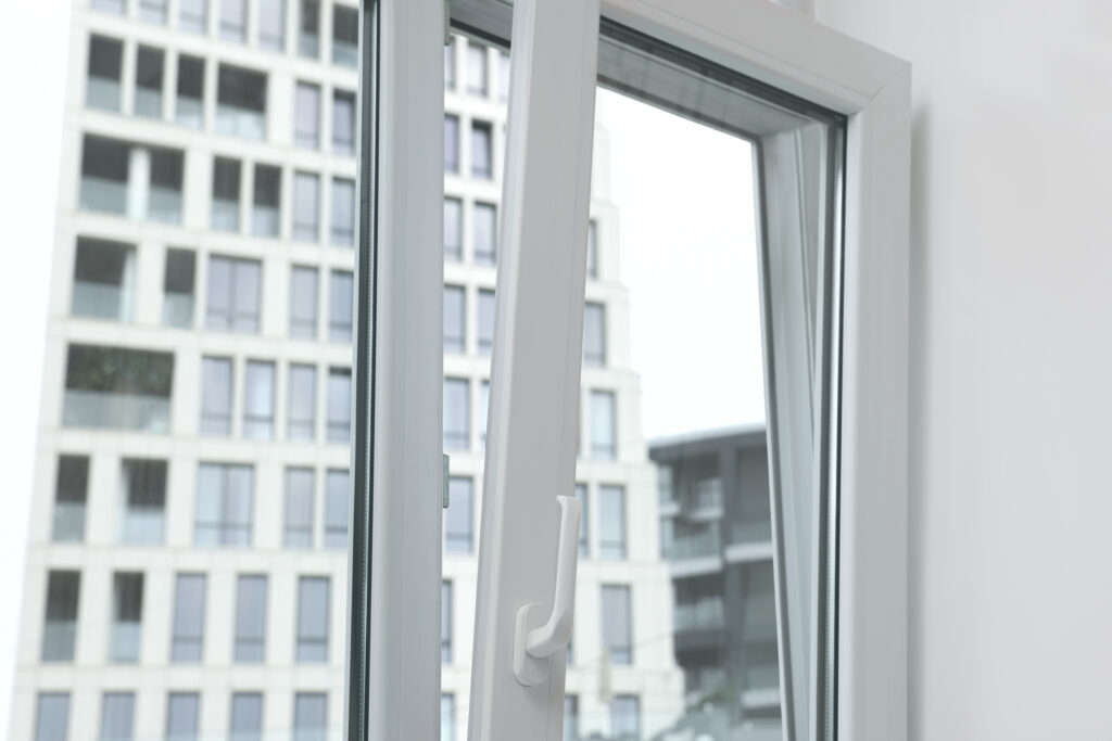 A white-framed window partially open inwards, revealing a modern, glass-covered building.