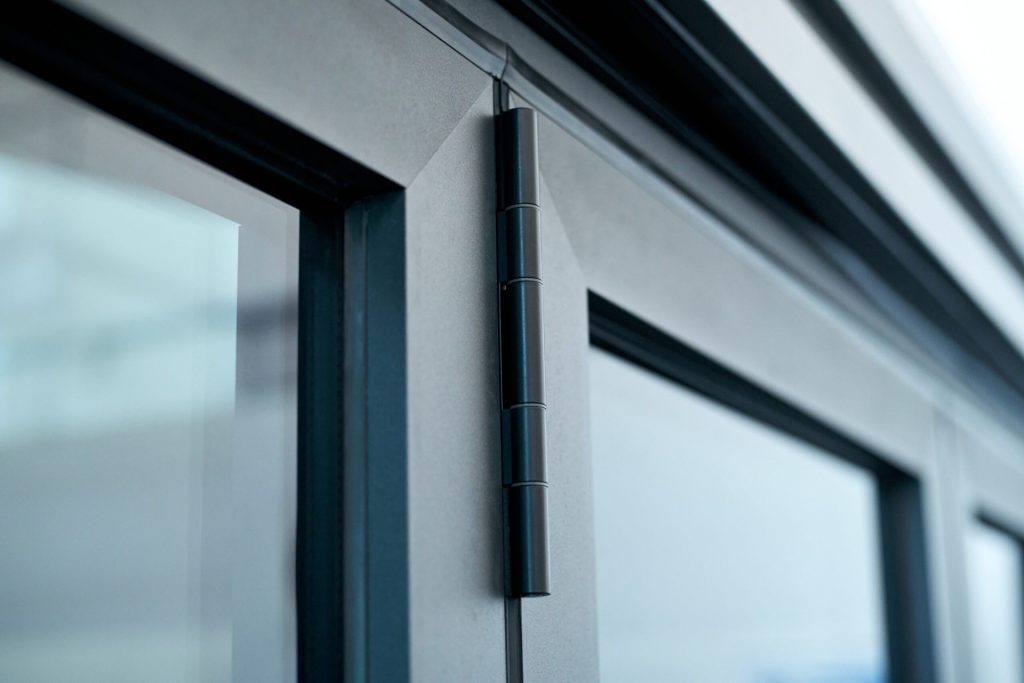 Close-up of a modern, black metal hinge on a sleek, gray-framed door.