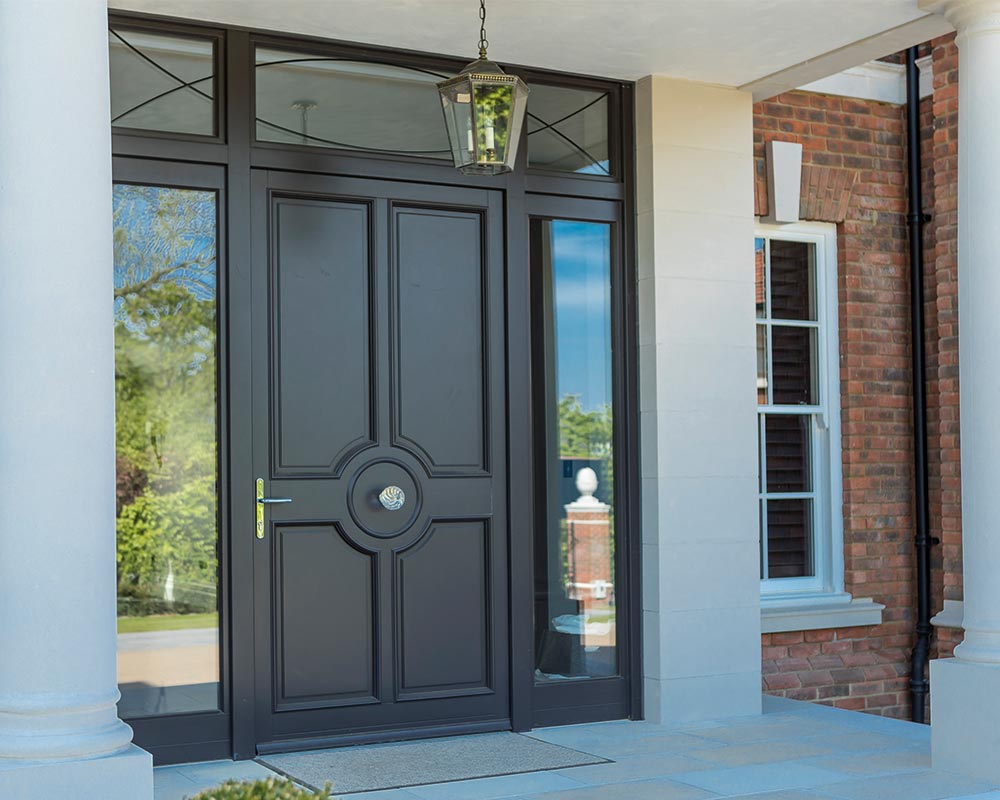 Black paneled front door with side windows, framed by white columns and brick walls. A lantern hangs above, creating a classic and welcoming entrance.