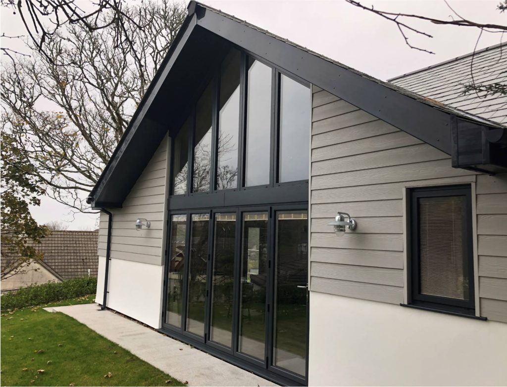 Modern house exterior with a gable roof and large glass windows. Grey siding doors and a small lawn convey a sleek, contemporary design.